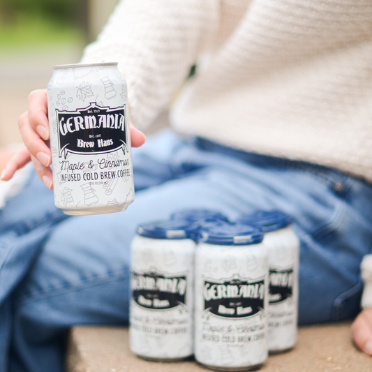 Person holding a can of Germania coffee with three more cans on a stone surface.