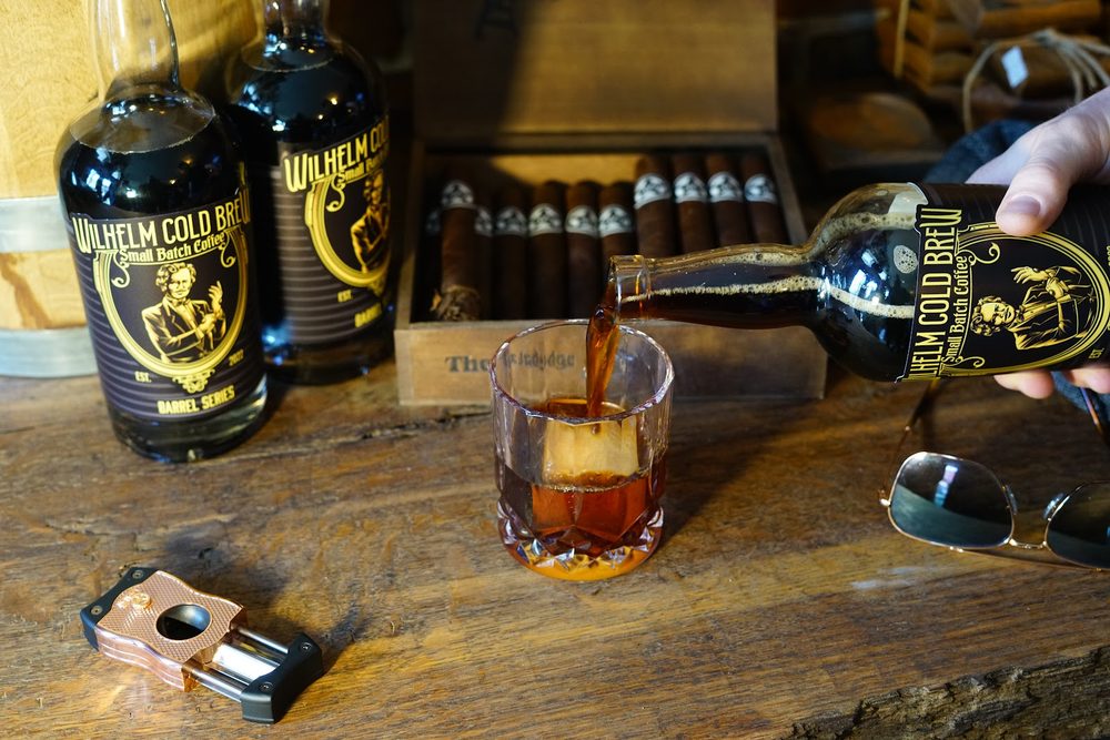 Pouring Wilhelm Cold Brew over ice beside a box of cigars